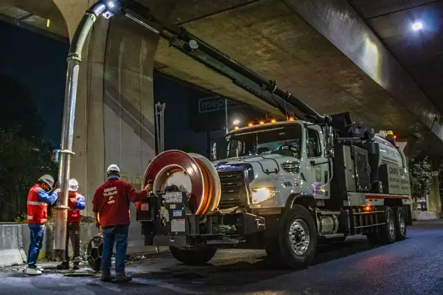 Equipe operando caminhão de vácuo em serviço de manutenção urbana durante a noite